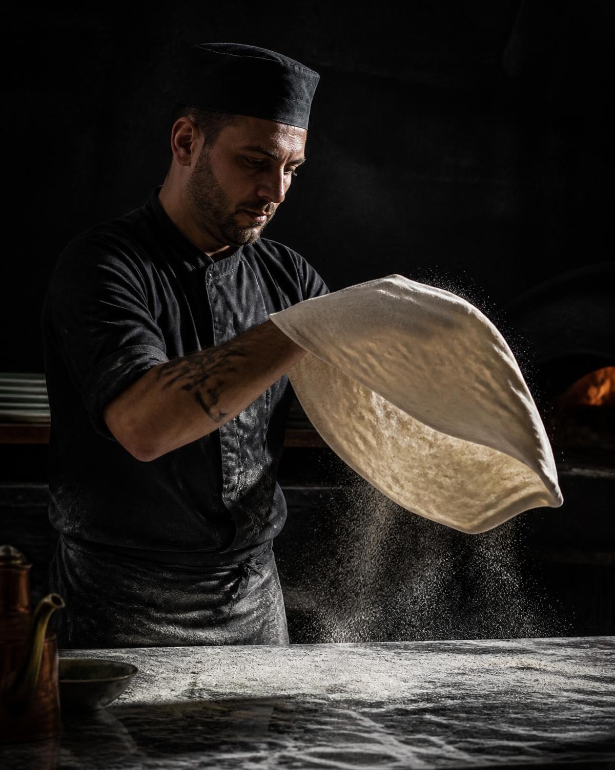 Pizzaiolo estirando la masa a mano en el obrador
